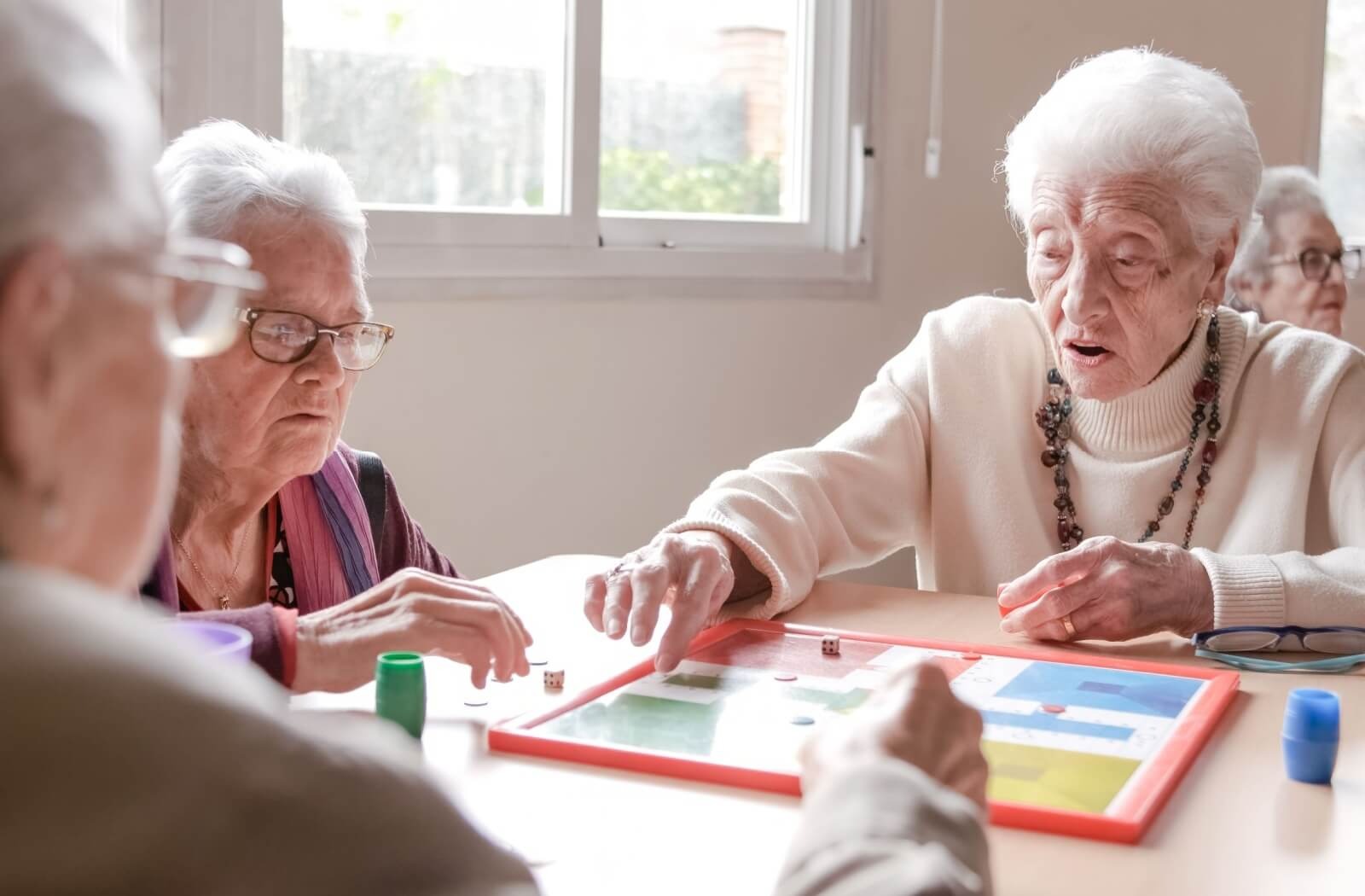 A group of older friends in assisted living play a tabletop board game.