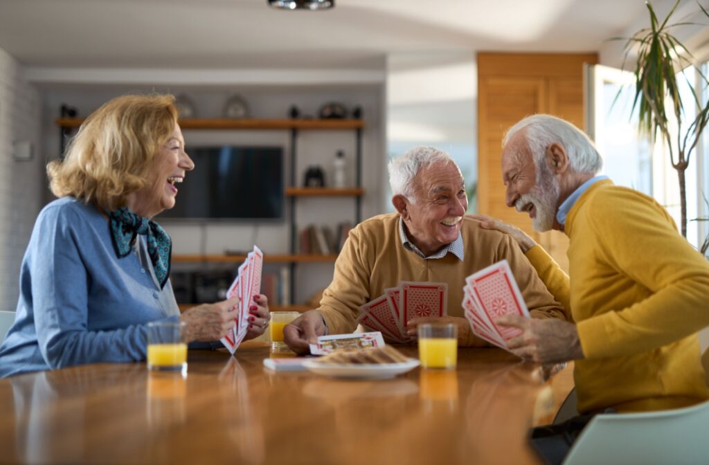 A group of senior friends in assisted living sit at the table playing a card game while drinking orange juice.
