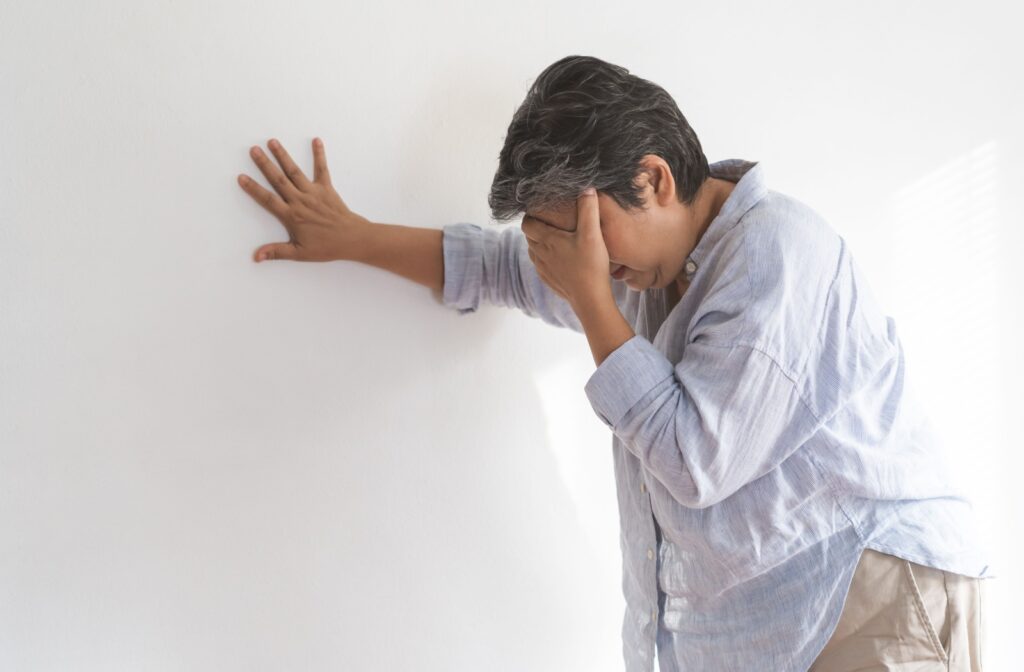 A senior covers their eyes with their hand as they lean against a wall.