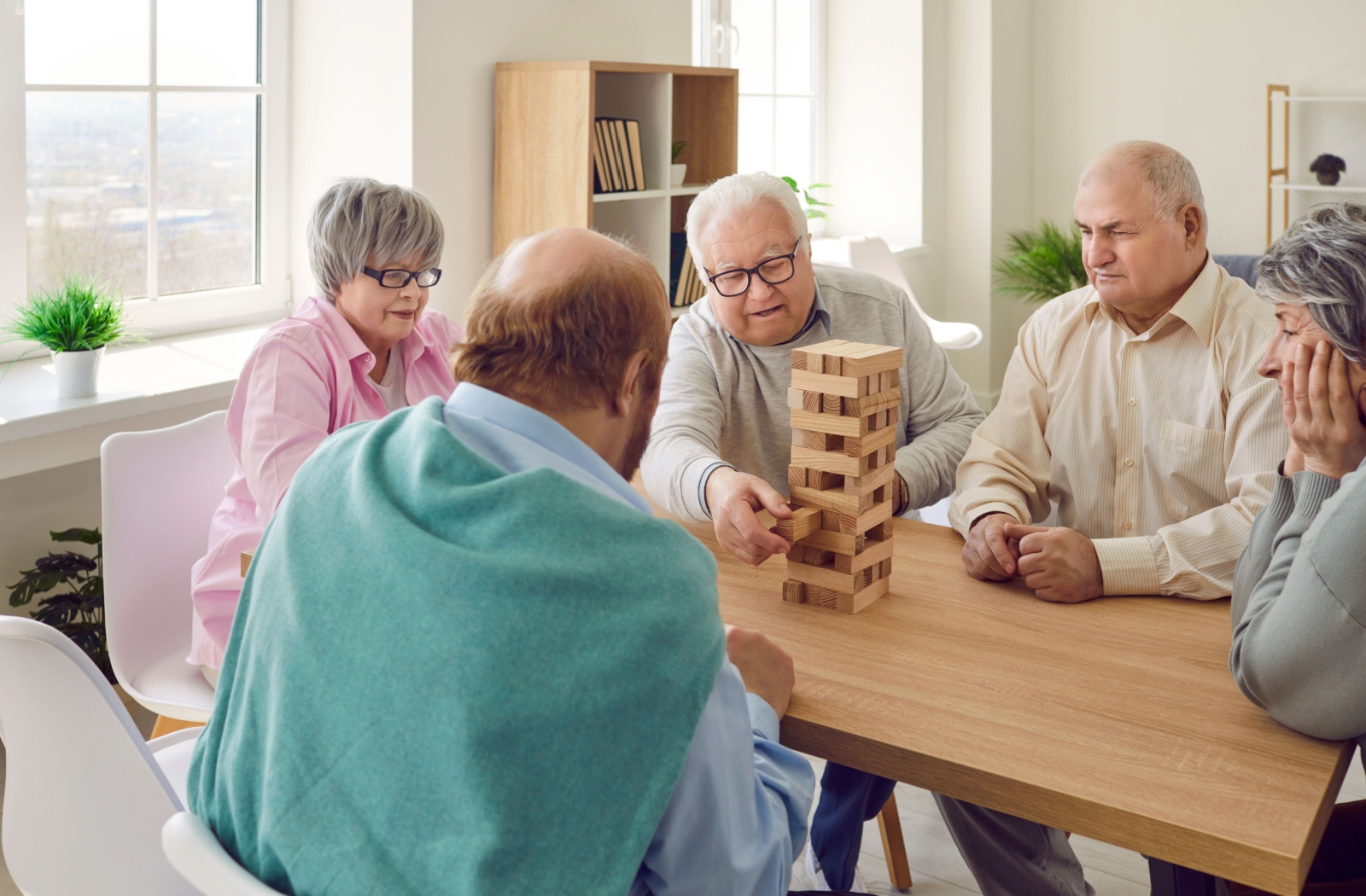 A group of senior friends in assisted living play a game of Jenga while sitting at a table.