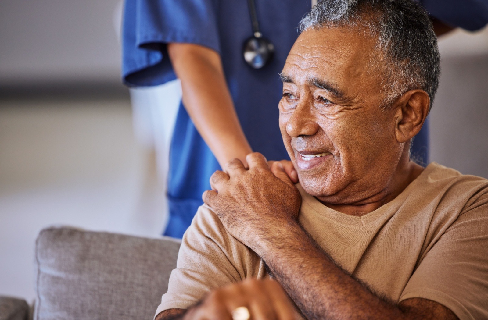 A caregiver rests their hand on a smiling senior's shoulder.